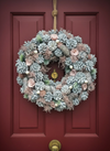 `#detail-photo`
Rustic artificial Christmas wreath crafted from real pinecones with a snowy finish, displayed on a dark wood front door.